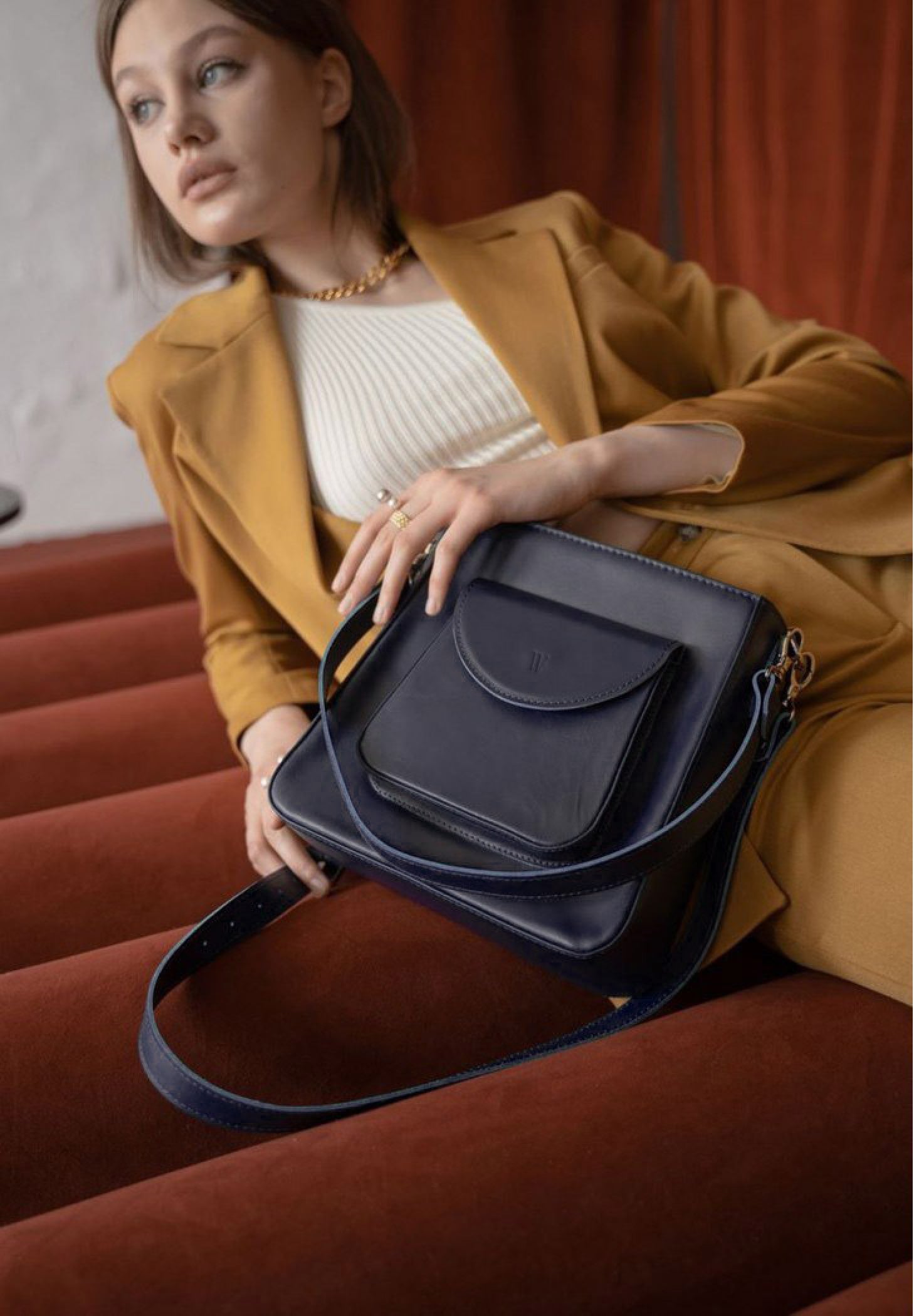 a beautiful woman is lying on the sofa and holding a high quality leather bag for women in navy blue color